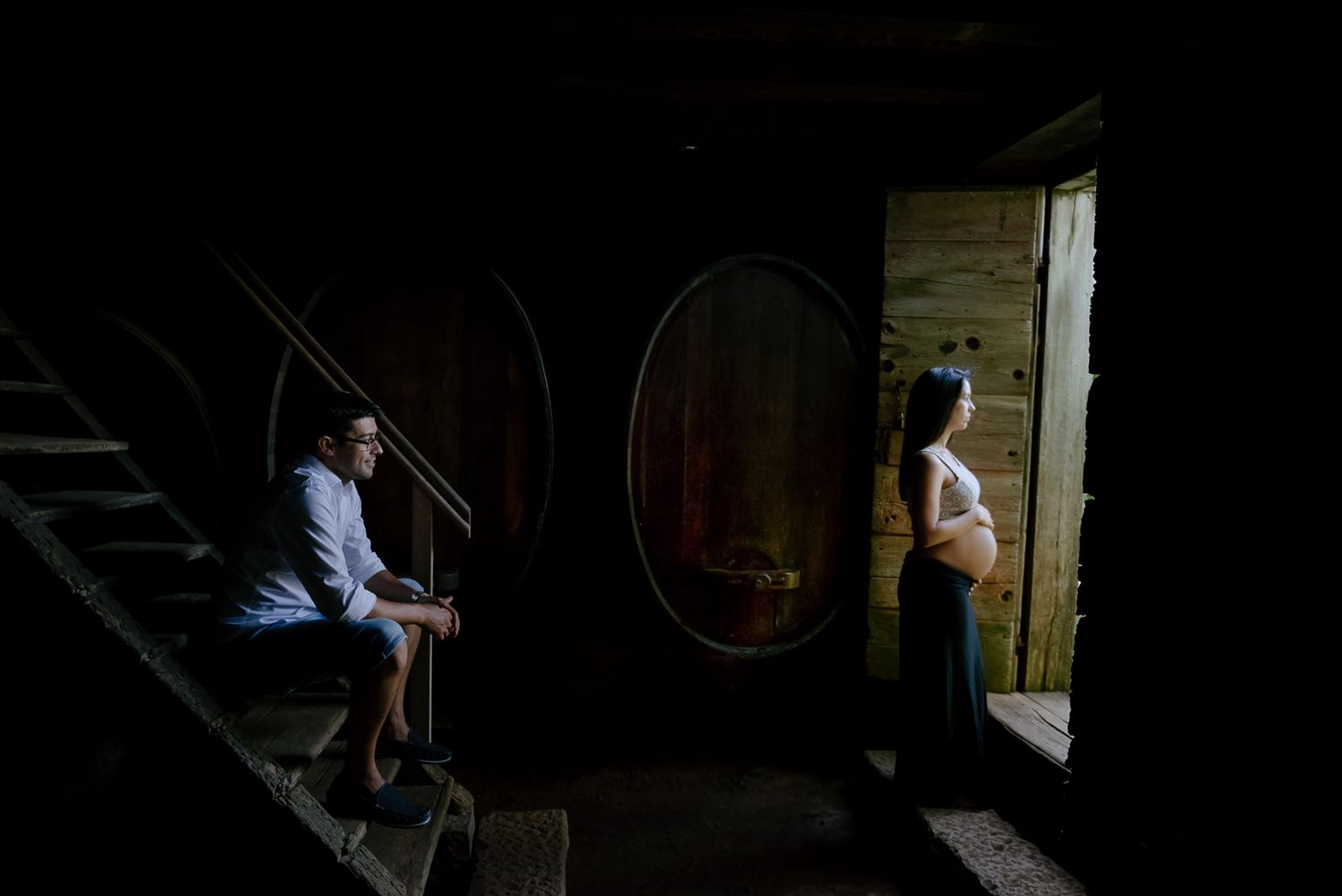 A moody indoor maternity scene with natural light streaming through a doorway.