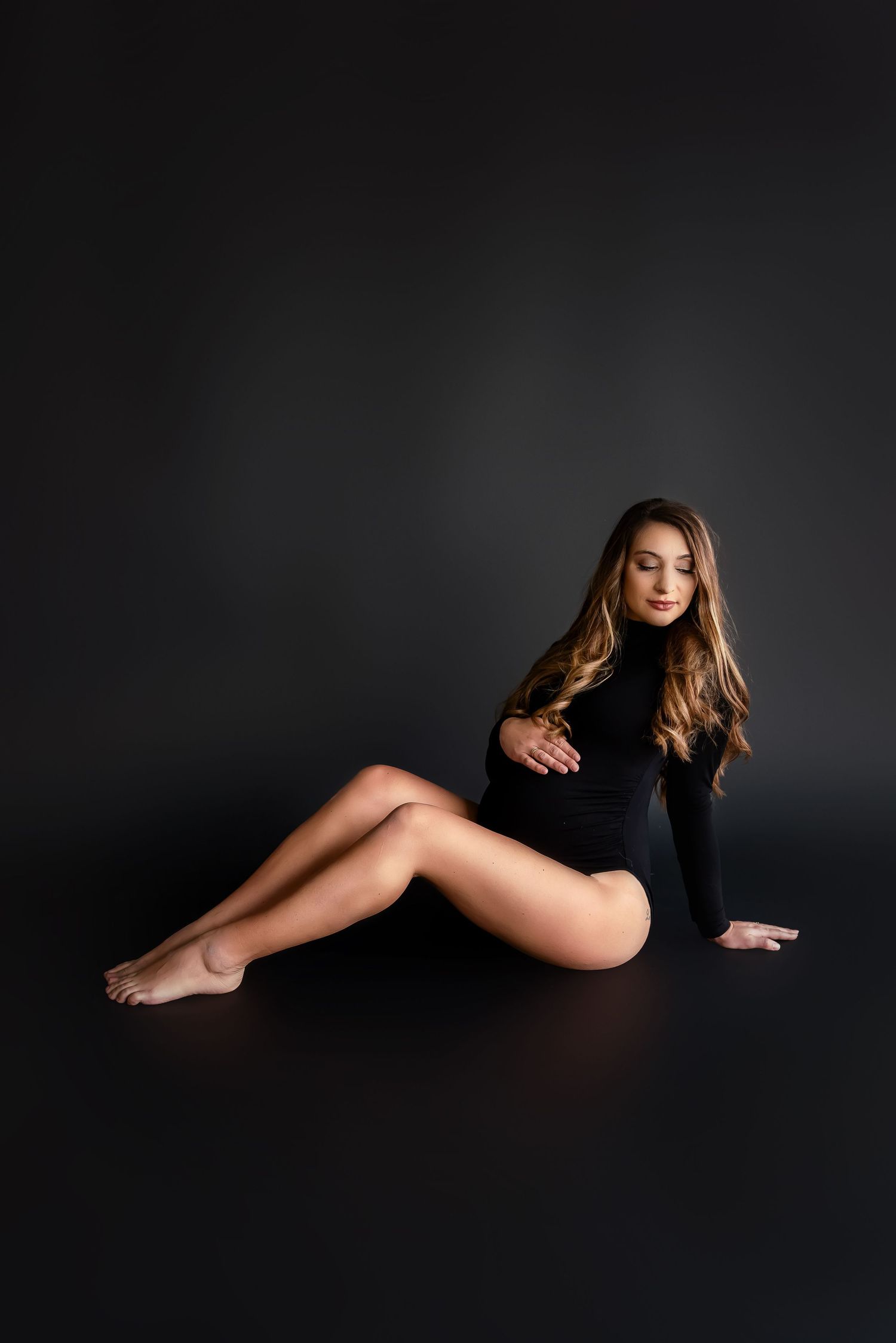 Artistic black and white maternity portrait with minimalist styling on dark background.