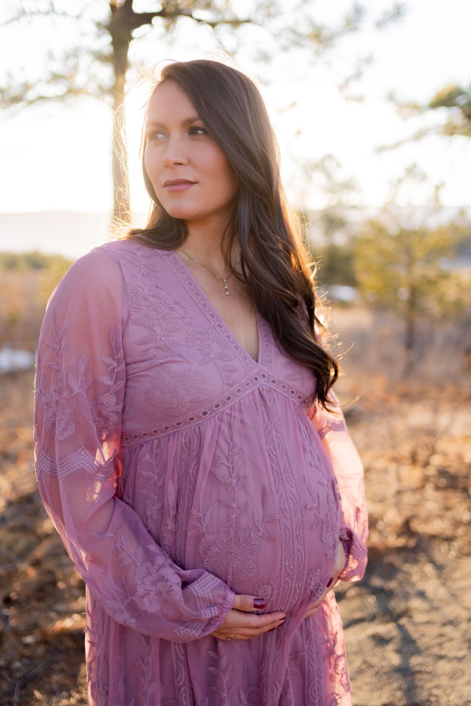 A sunset maternity portrait in a mauve dress with golden backlight through trees.