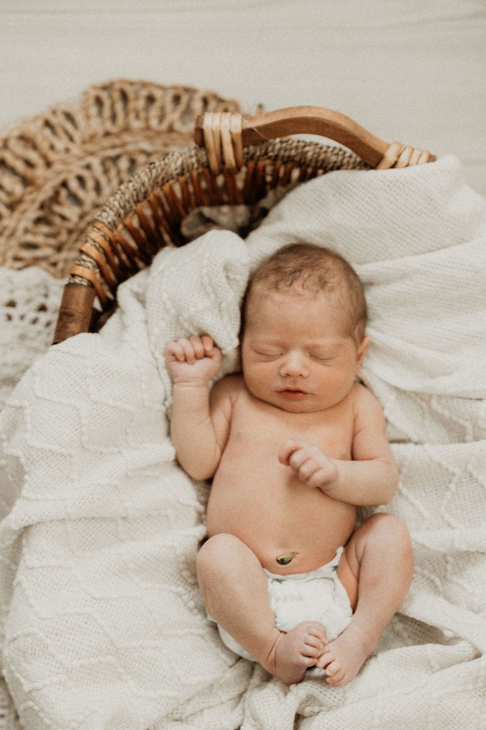 Sleeping newborn baby peacefully resting on white blanket in woven basket.