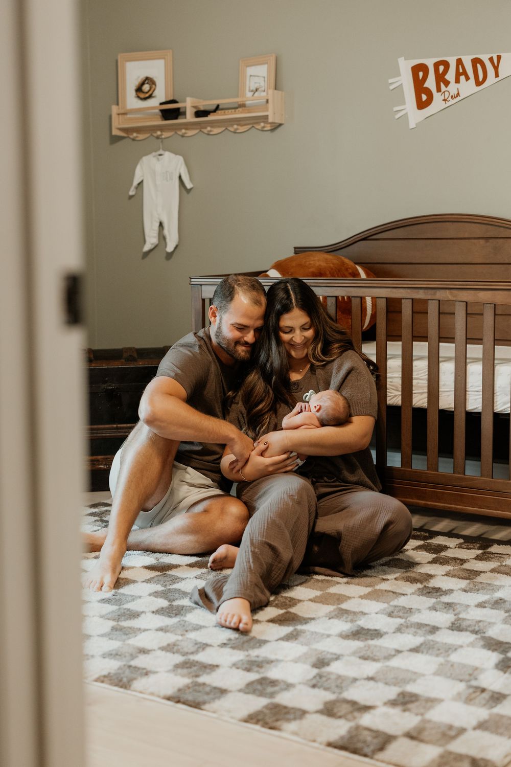 Family sharing intimate moments in nursery room with wooden crib and checkered rug.