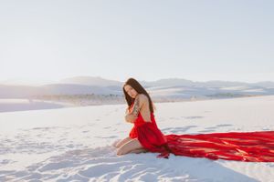 A figure in a flowing red dress sits gracefully against a stark white desert landscape.