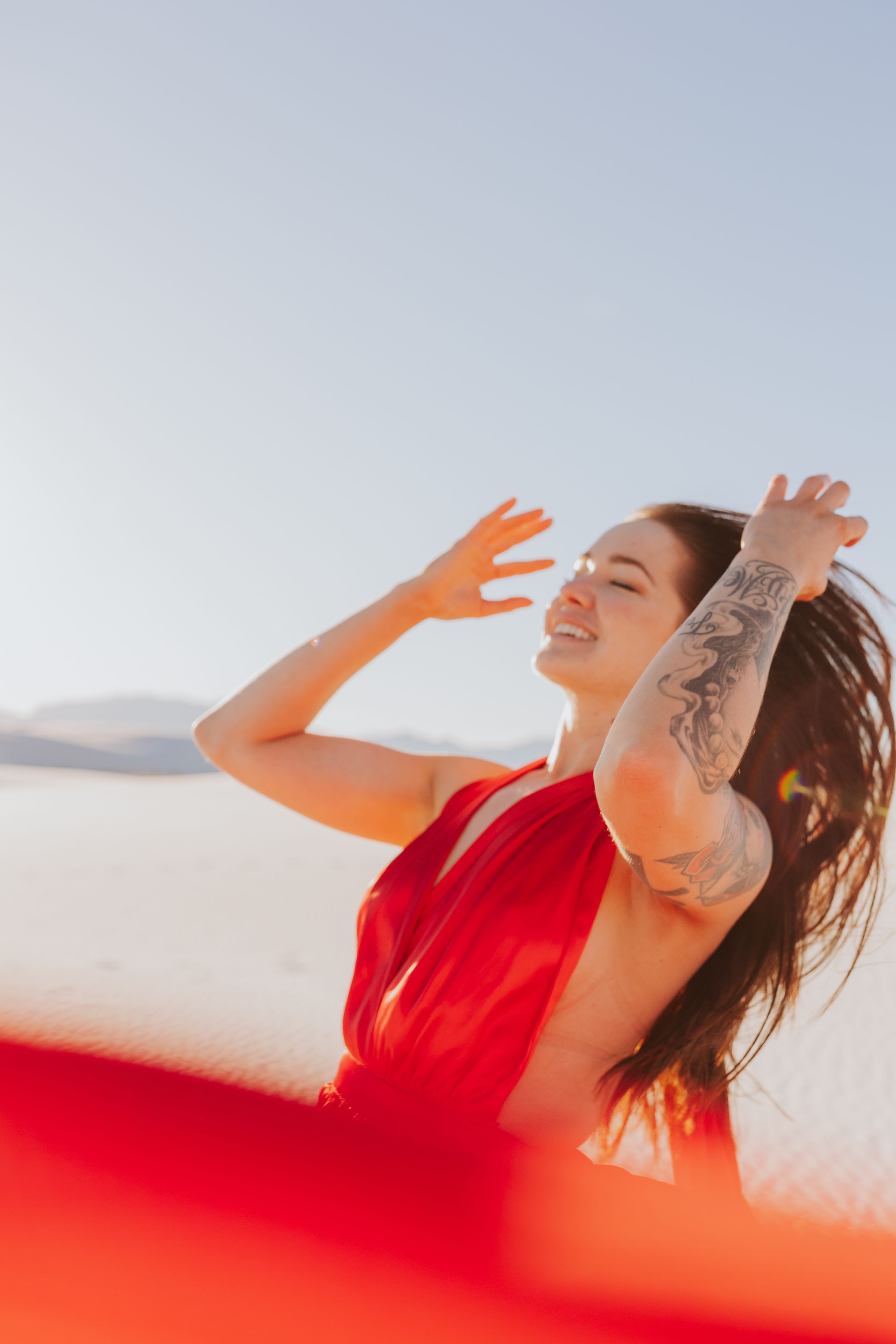 Woman in red dress posing dramatically against bright sky.