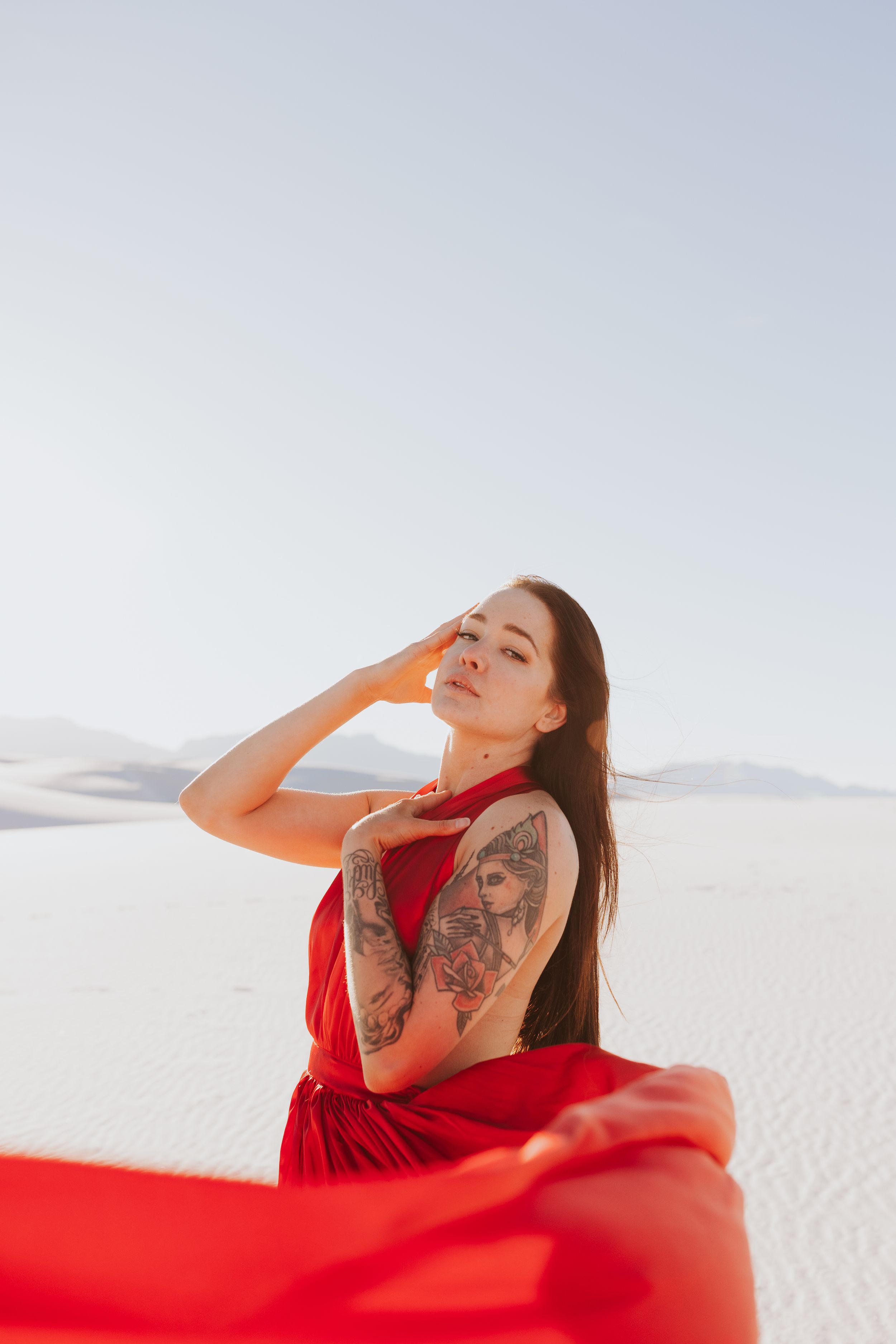 Woman in flowing red dress posing on white sand dunes.
