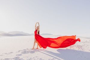 Red fabric flowing in the wind against white sand dunes landscape.