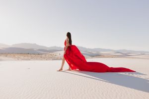 Red fabric billows dramatically across pristine white sand with mountains in the background.