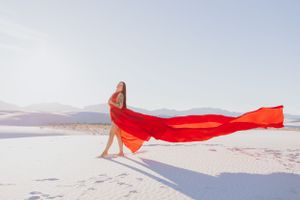 Vibrant red fabric flows across a stark white sand landscape under clear blue skies.
