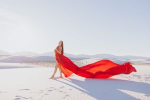 Flowing red fabric creates striking contrast against white sand dunes in a desert landscape.