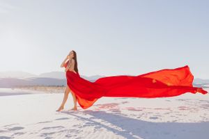 A dramatic scene of red fabric dancing across white sand with mountains on the horizon.