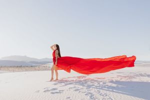 Red fabric catches wind against pristine white sand dunes in an artistic desert photo.