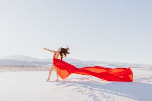Bright red fabric creates movement and drama against stark white desert sand.