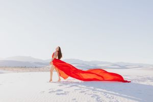 A striking composition of flowing red fabric against white sand and mountain backdrop.