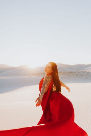 A flowing red dress billows in the desert wind as sunlight bathes the white sand dunes in golden light.