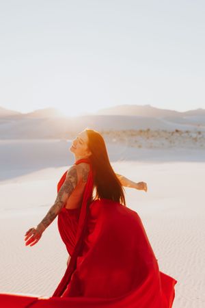 A red dress flows dramatically against white sand dunes during a desert photoshoot at sunset.