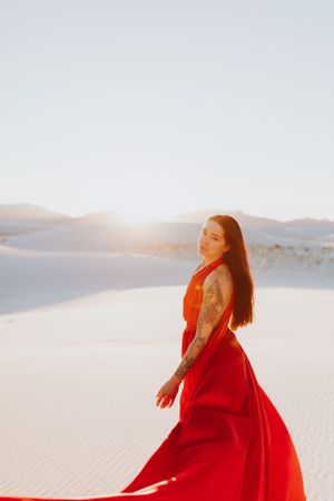 Long red dress contrasts beautifully against pristine white sand dunes in ethereal desert landscape.