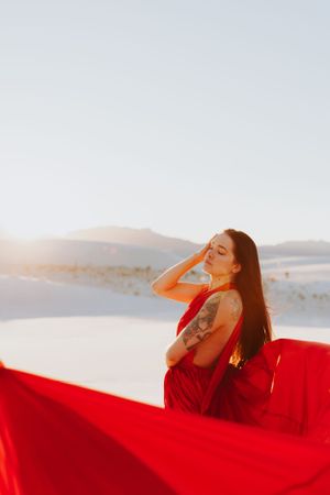 Dramatic red gown creates striking contrast against white sand dunes during golden hour photoshoot.