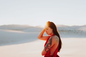 Ethereal desert photography featuring flowing red dress against stark white sand dunes at sunset.
