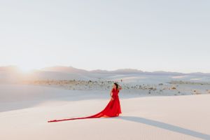 Minimalist desert scene with flowing red dress creating dramatic lines across white sand.