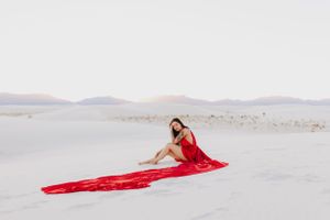 Dreamy desert photography with flowing red fabric against pristine white sand dunes.