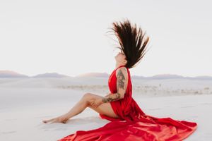 Dynamic movement captured in red dress against stark white desert landscape at sunset.