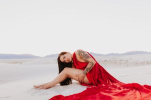 Artistic desert photography featuring flowing red fabric against stark white sand and mountain backdrop.