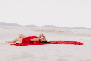 Minimalist desert fashion photography with red fabric against pale sand and distant mountains.