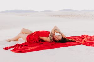 Fashion photograph showcasing red fabric dramatically arranged on desert sand with mountain backdrop.