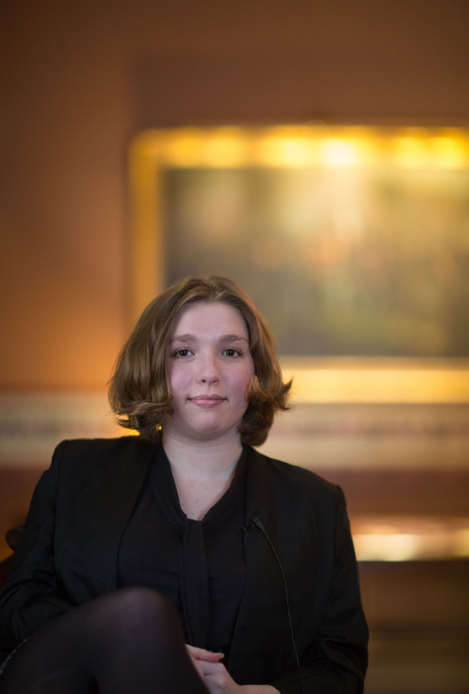 Portrait of legislative intern in formal black attire against warm brown studio background.
