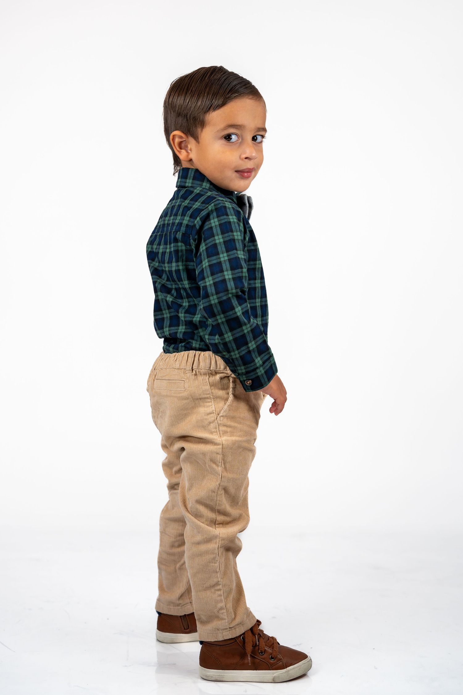 Young model in plaid shirt and khaki pants poses sideways against white background.