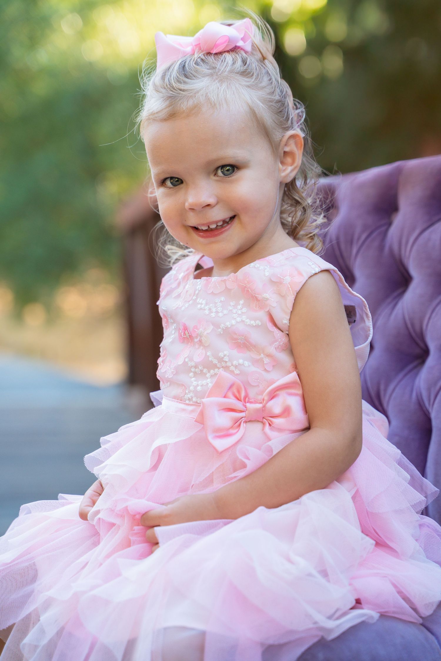 A child wearing a fluffy pink tulle dress with bow details sits outdoors in a garden setting.