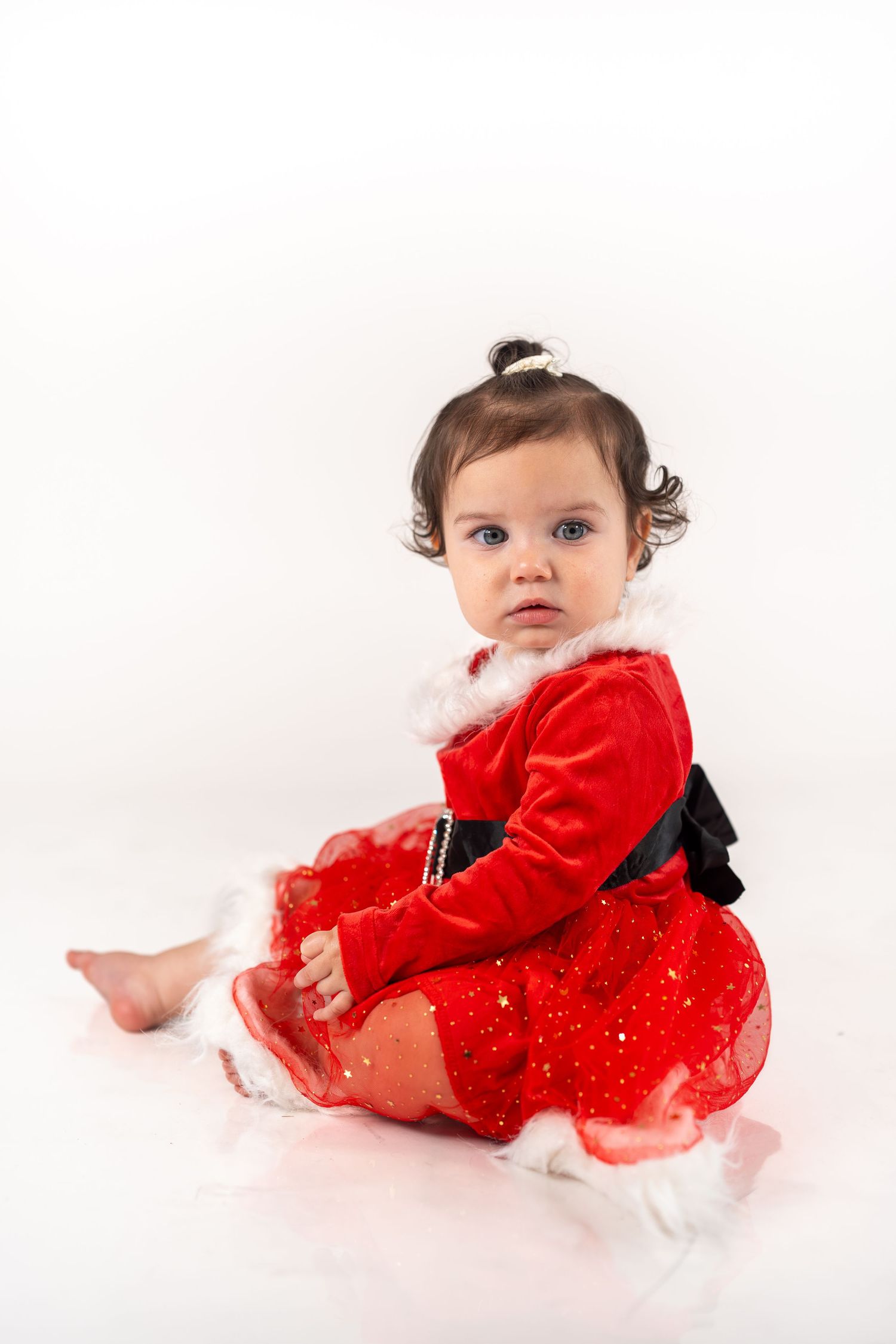 A baby in a sparkly red holiday dress crawls and poses on a white background in a photo series.