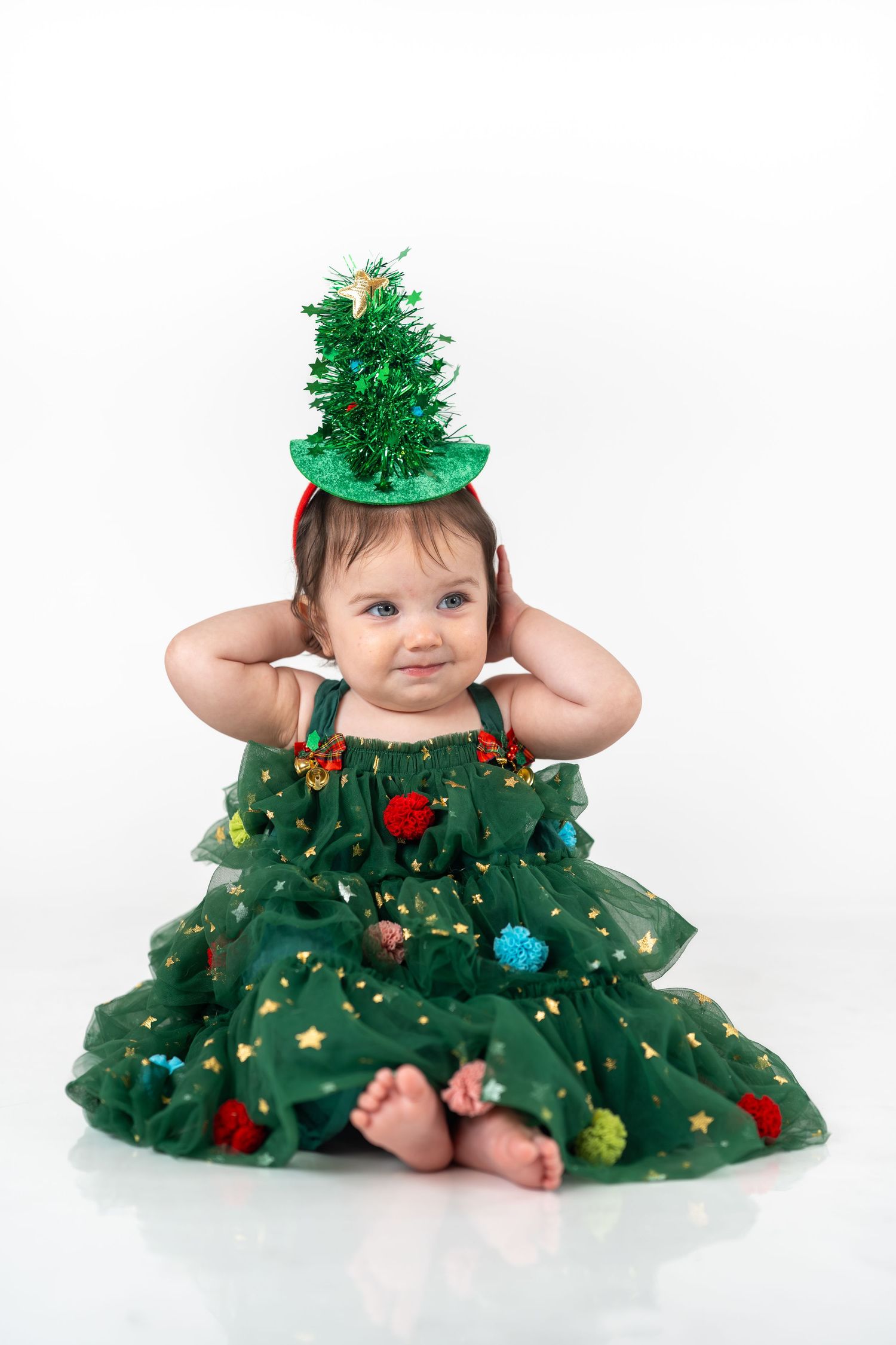 A baby wearing a festive green Christmas tree tutu dress with ornaments poses for three holiday photos.