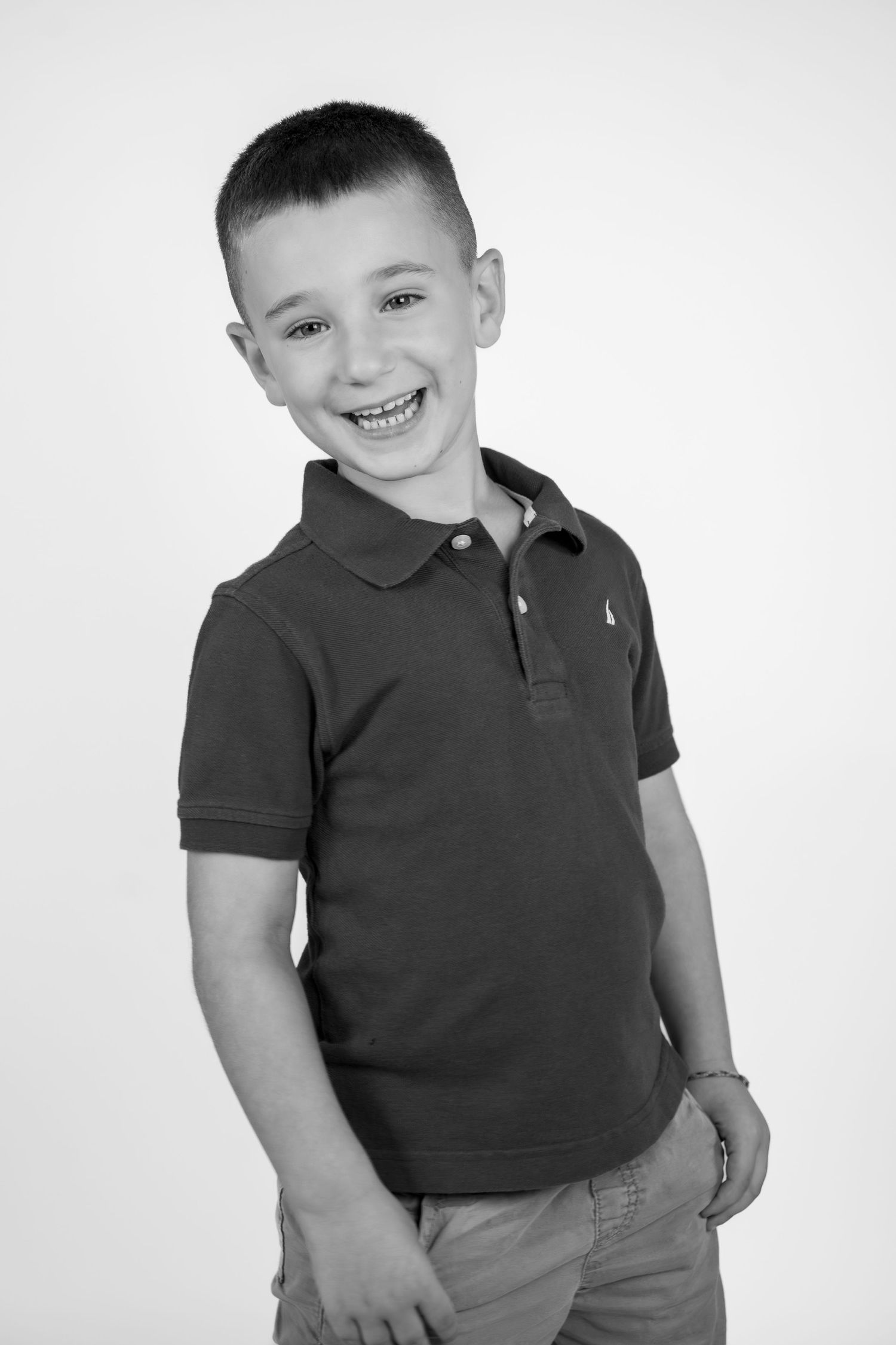 Three black and white portraits of a smiling young child in a dark polo shirt and casual attire striking playful poses.