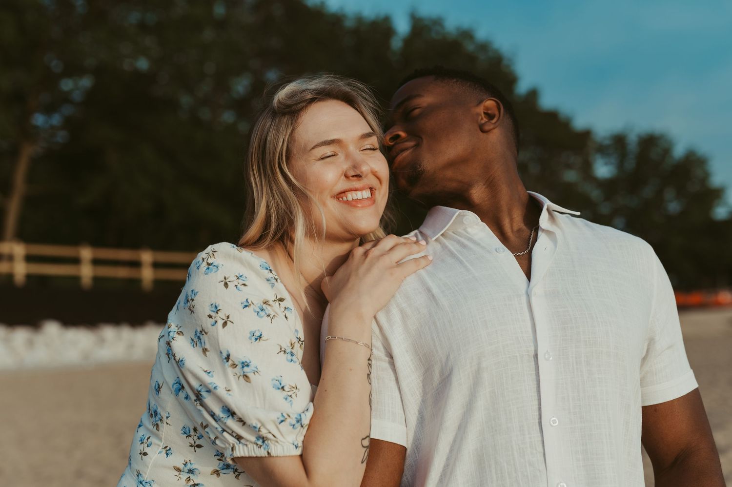 A happy couple sharing a tender moment on a beach, with the man kissing the smiling woman's cheek.