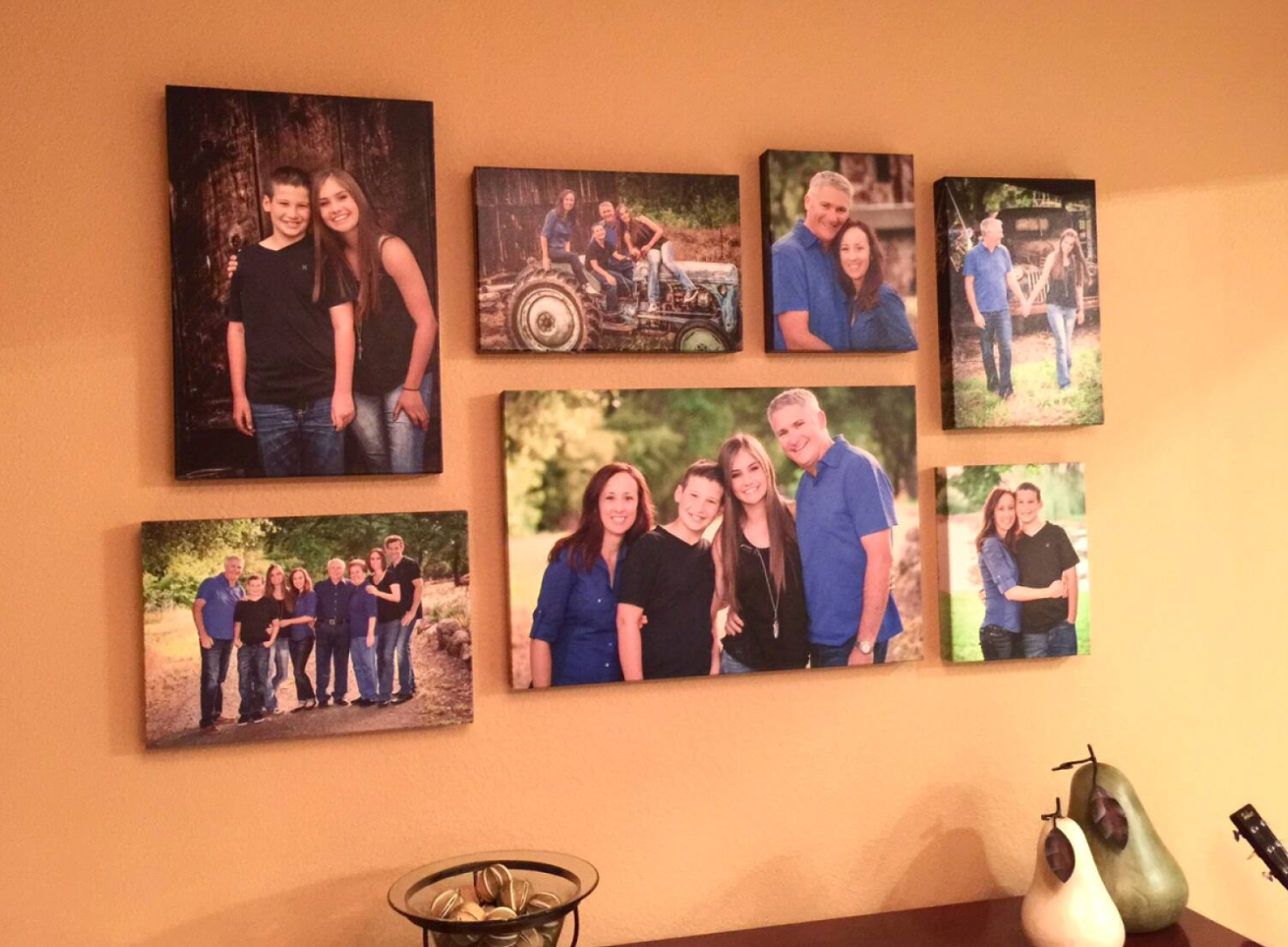 Family photo gallery wall with multiple canvas prints arranged on orange wall.