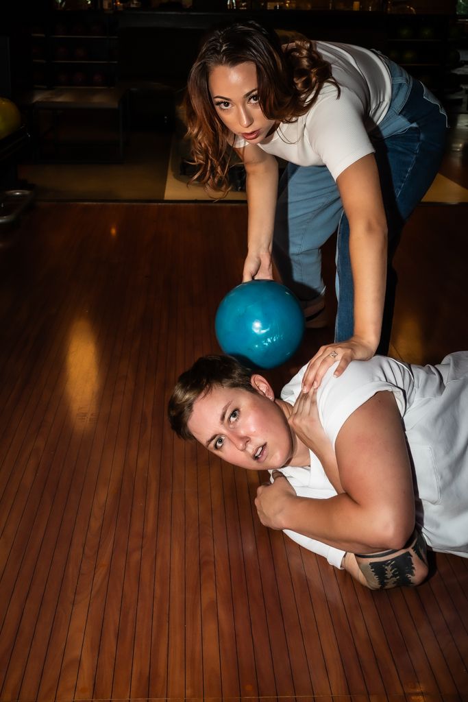 Scripted image of a woman pretending to bowl while another woman lays in her path with a worried look on her face