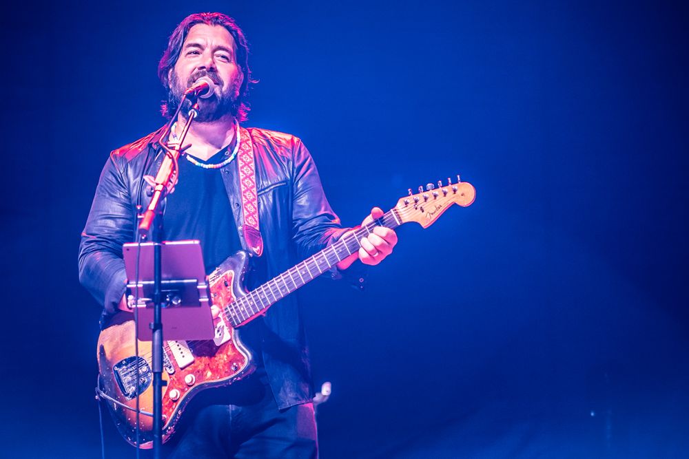 Image with a blueish hue of musician on stage playing guitar and singing