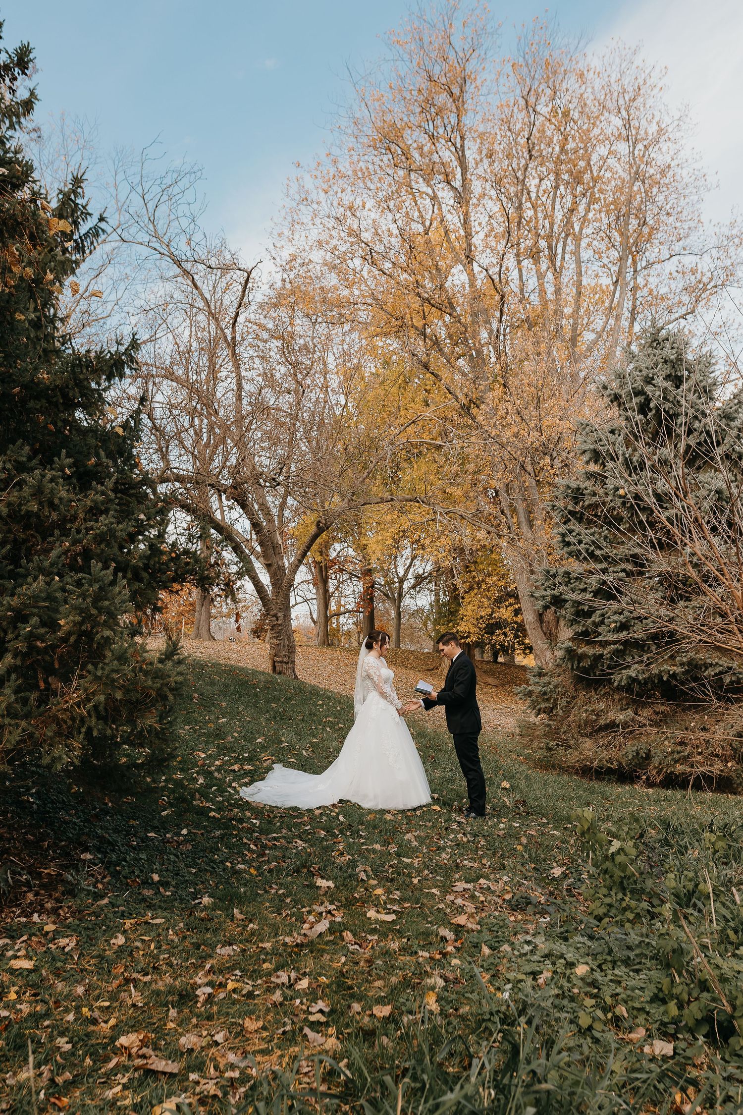 Newlyweds walk hand in hand through autumn trees with flowing white wedding dress.