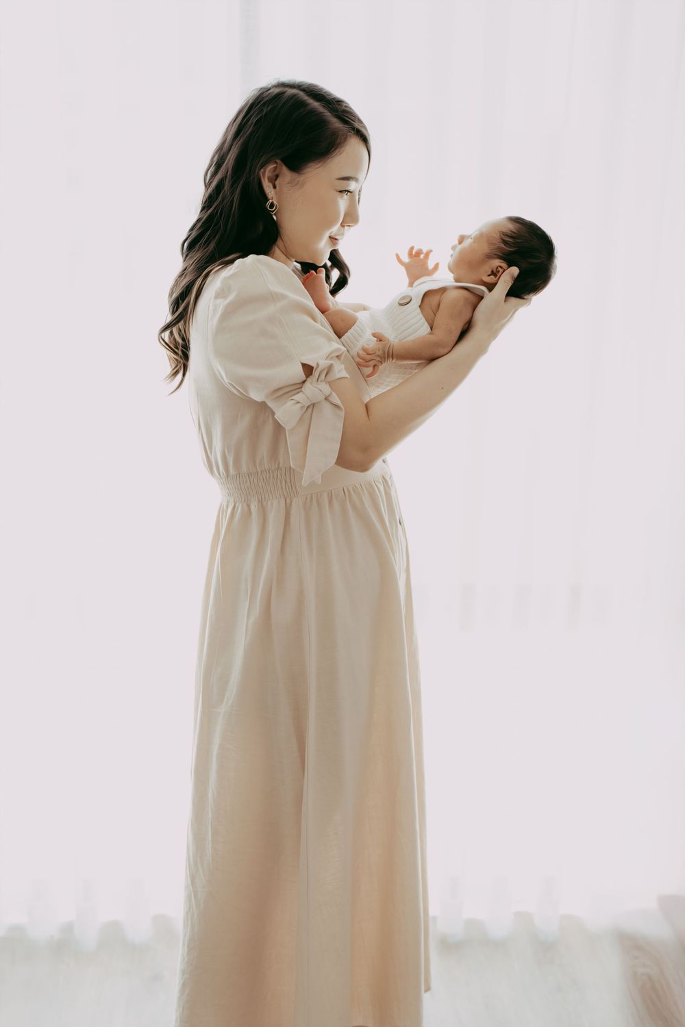 Parent in cream dress holding and bonding with newborn baby against white background.