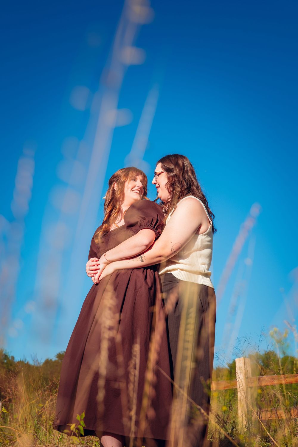Two figures embrace against a bright blue sky with tall grass in the foreground.