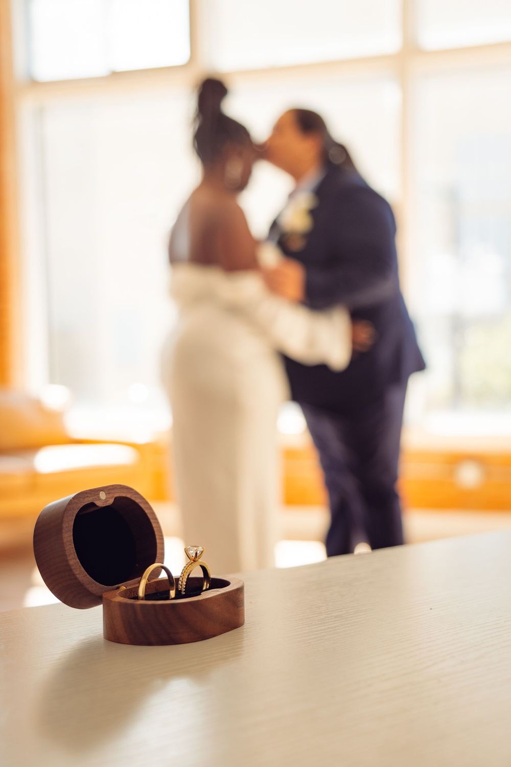Wedding rings in wooden box with couple silhouetted in background.