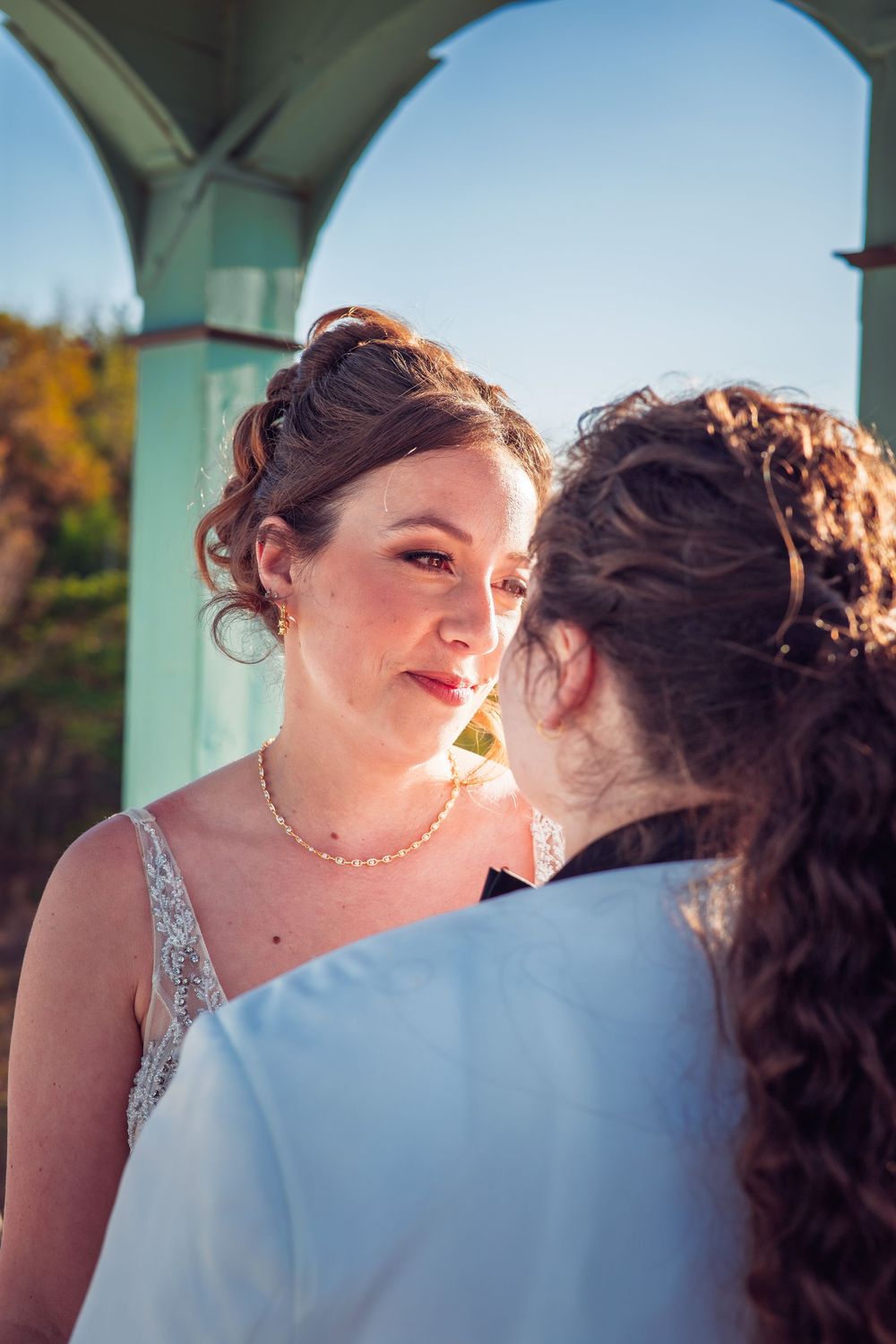 A romantic wedding portrait captured under a green gazebo on a sunny autumn day.