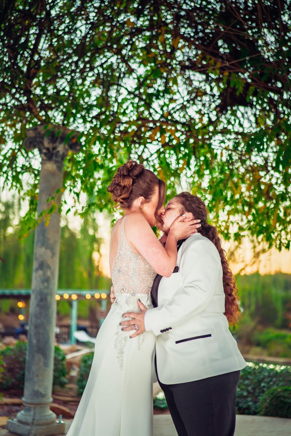 An intimate wedding portrait captured under a canopy of trees with dappled sunlight.