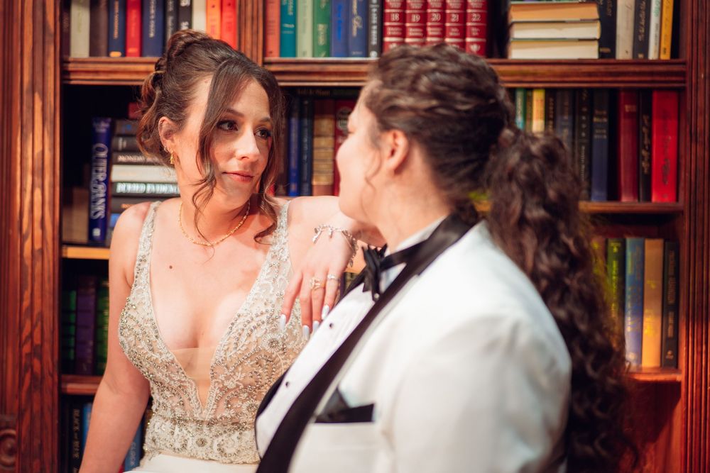 A romantic wedding portrait taken in a library with colorful bookshelves as backdrop.