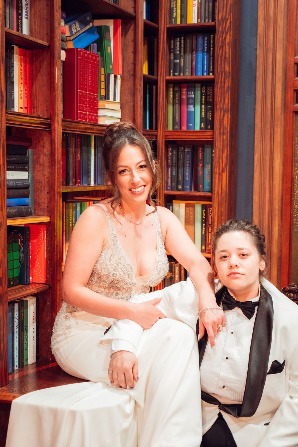 A relaxed wedding portrait in a library with wooden bookshelves filled with colorful books.