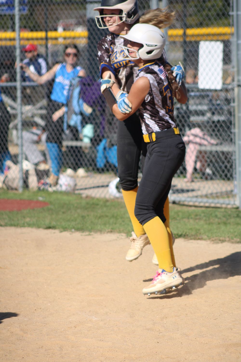 Softball player in yellow socks and black uniform running on dirt field.