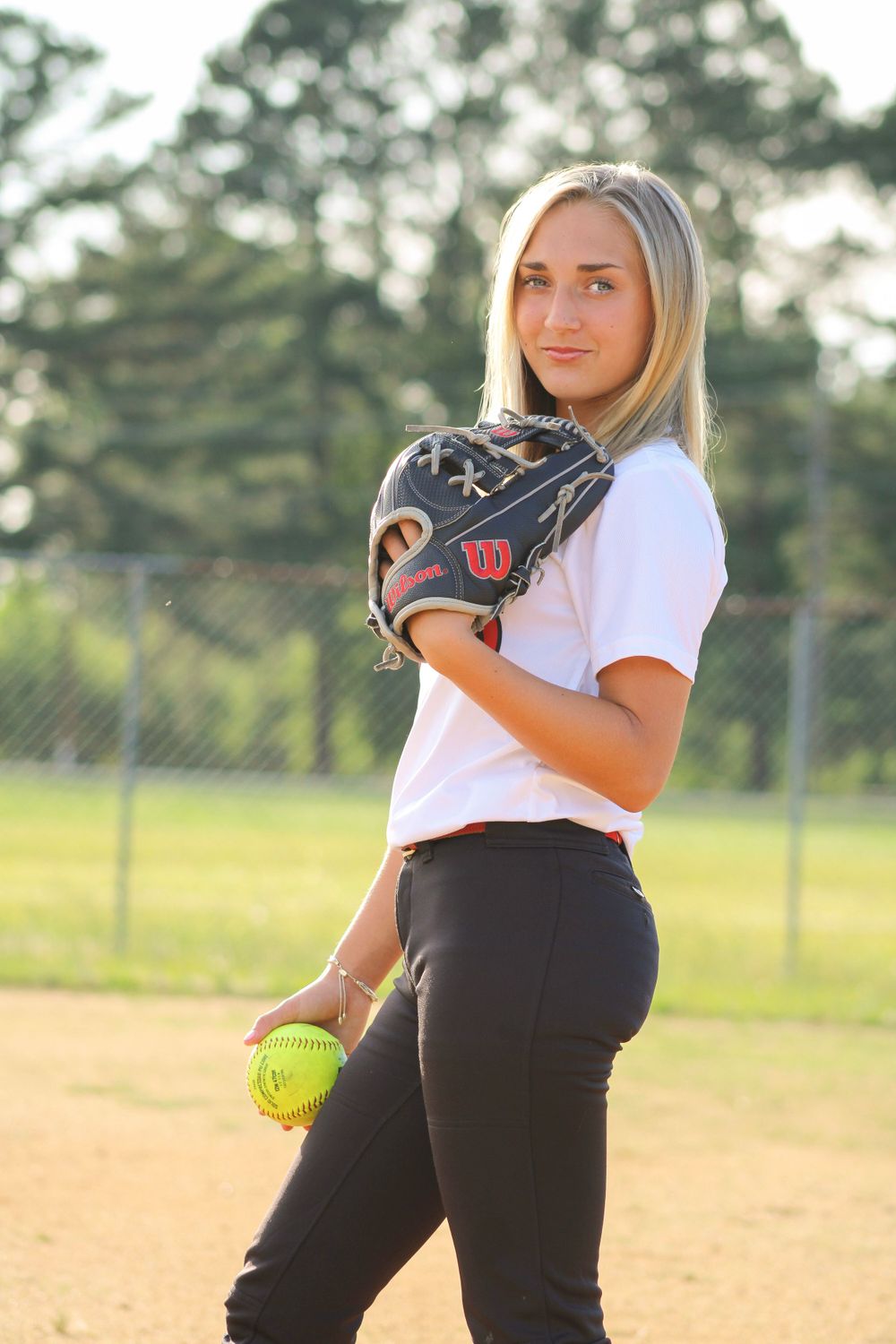 Softball player in white uniform and black pants practicing on baseball field.