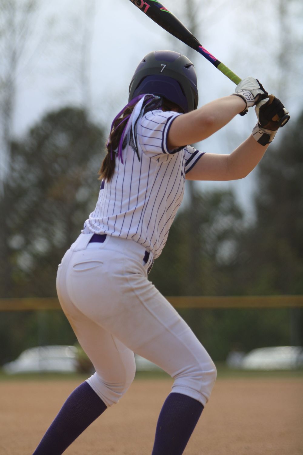 A softball batter in pinstripe uniform stands at the plate ready to swing.