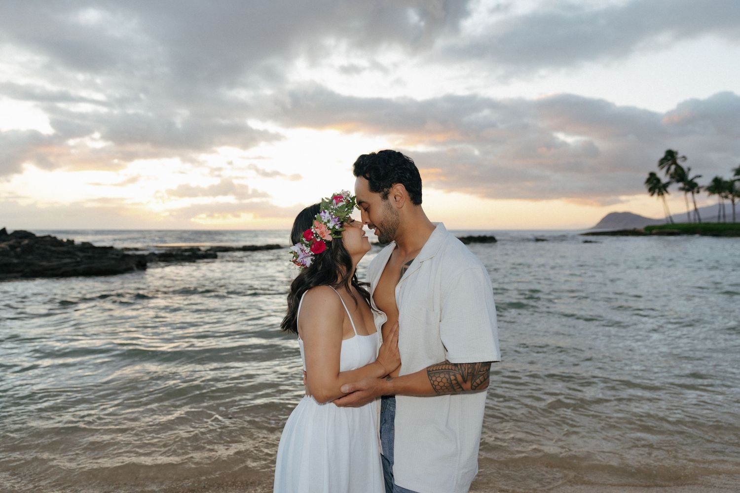 Romantic beach photoshoot at sunset with ocean and palm trees in background.