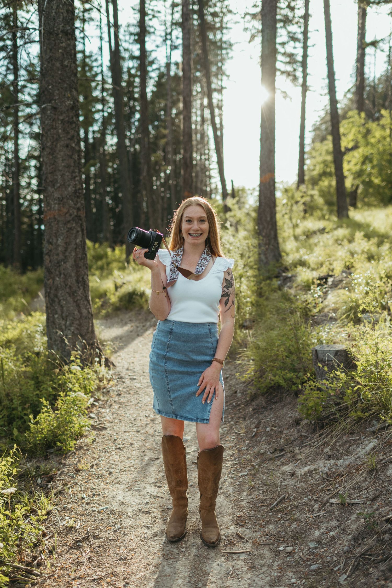 A photographer stands on rocky shoreline holding camera equipment with a frozen lake and forest in background.